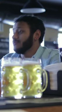 Ilık ışıkla dolu canlı bir barda, iki neşeli genç adam soğuk bira bardakları üzerine kahkaha ve ilgi çekici hikayeler paylaşıyor. Canlı atmosfer yoldaşlık ve kutlama yayıyor, dostluğun özünü yakalıyorlar.