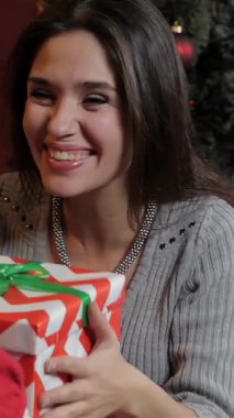 Işıl ışıl beyaz bir kadın, kızı ona şaşırtıcı bir şekilde paketlenmiş bir Noel hediyesi verirken neşeyle parlıyor. Işıldayan bir ağaç ve canlı süslemelerle bezenmiş samimi oturma odası, sıcaklık ve sevgi yayar, tatilin ruhunu mükemmel bir şekilde yakalar.