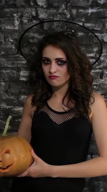 Gösterişli siyah kıyafetli büyüleyici bir kadın büyücü neşeli bir sırıtışla oyulmuş bir balkabağı tutuyor, desenli siyah tuğla bir duvara dayanıyor. Cadılar Bayramı 'ndan esinlenilmiş bu sahnede büyüleyici bir gizem ve sihir havası yayılıyor.