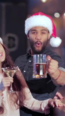 Coşkulu, çoklu etnik arkadaşlardan oluşan, Noel Baba şapkalı neşeli bir grup bardaklarını coşkulu bir şekilde kaldırıyorlar. En sevdikleri futbol takımına tezahürat ederken elektrik atmosferi heyecanla uğulduyor.