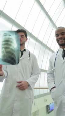 Parlak, modern bir tıbbi tesiste, temiz beyaz önlük giyen iki kendine güvenen erkek doktor akciğer röntgenini yakından inceleyerek sigara içmenin tehlikelerini vurguluyor. Odaklanmış ifadeleri ve profesyonel tavırları derin bir bağlılığı yansıtıyor.