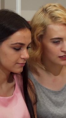 İki hayat dolu genç kadın, biri dalgalı siyah saçlı, diğeri şık sarı dalgalı, bir dizüstü bilgisayarda zevkle iş birliği yapıyorlar, sıcaklık ve yaratıcılık saçıyorlar. Bulaşıcı kahkahaları ve parlak gülümsemeleri çalışma alanını aydınlatıyor.