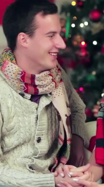 Sıcak, Noel dekore edilmiş bir odada, sıcak süveter ve renkli eşarplar giyen büyüleyici bir çift, sevgi saçan içten hediyeler vererek hoş bir anı paylaşıyorlar. Işıldayan gülümsemeleri ve şefkatli bakışları büyülü bir atmosfer yaratarak,