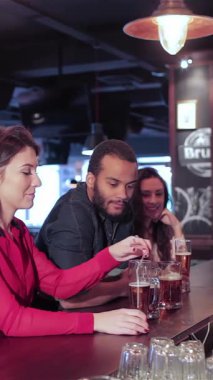 İki neşeli kadın ve bir erkeğin yer aldığı canlı bir yetişkin üçlüsü, barda bir gece eğleniyor, kahkahalar atıyor ve bardaklarını tokuşturuyor. Barmen ustalıkla biraları tazelerken, arkadaşları en sevdikleri futbol takımı için tezahürat yapıyor.