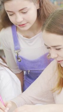 Üç şevkli genç kız renkli kitaplıklarla çevrili canlı bir kampüs kütüphanesinde ortak bir projeye daldılar. Bulaşıcı kahkahaları ve ortak fikirleri arkadaşlığın ve takım çalışmasının özünü yayıyor.