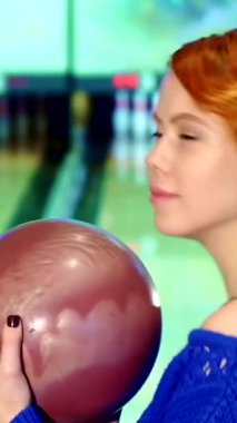 Neşeli, kızıl saçlı, neşeli beyaz bir kızın canlı bir yakın çekimi. Güçlü atışını serbest bırakmaya hazırlanırken kendine güvenen bir bowling topunu tutuyor. Işıl ışıl gülüşü ve ışıl ışıl gözleri Oyunun heyecanını yakalıyor