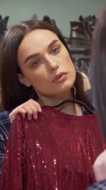 Güzel genç bir kadın aynanın önünde elinde iki göz kamaştırıcı elbise tutarak şık bir butikte şık seçimini derin derin düşünüyor. Giysilerin zengin dokuları ve canlı renkleri onun kusursuz moda anlayışını yansıtıyor ve bunu değiştiriyor.