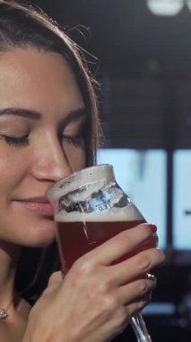 Uzun, dalgalı saçları olan çekici bir kadın köpüklü bir bira tutuyor. Işıl ışıl gülüşü, canlı bir bar atmosferinin keyfini çıkarırken saf mutluluğu yansıtıyor. Kırsal ahşap bar ve yumuşak, ılık ışıklandırma, gevşemek için mükemmel bir arka plan yaratır.