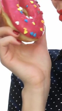 Lezzetli bir yakın plan, şık bir çörekle retro bir kızı dudaklarına canlı bir çörek getirirken yakalar. Çarpıcı kırmızı ruju ve puantiyeli tişörtü eski moda cazibesini yansıtıyor. Nostaljik ve tatlı bir hoşgörü anına davetiye çıkarıyor.