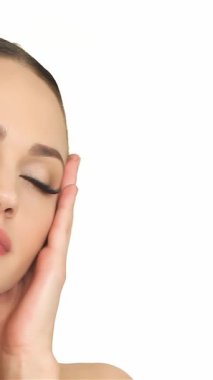 Bu büyüleyici yakın plan, beyaz bir kadının zarif bir şekilde yüzünü okşayarak zarafet ve sükunet saçtığını gösteriyor. Gözleri yavaşça kapalı ve huzurlu bir gülümseme ile saf beyaz bir kadına karşı güzellik ve kendine güveni somutlaştırır.