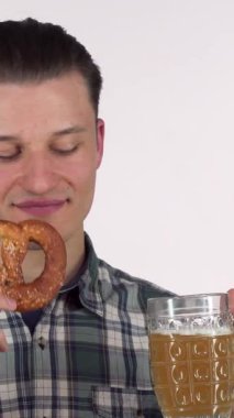 Şık ekose gömlekli neşeli bir genç adam ferahlatıcı bir biranın tadını çıkarıyor, elinde altın-kahverengi bir kraker tutarken anın tadını çıkarıyor. Bu canlı sahne, şenlikli toplantılar ve Ekim Festivali için mükemmel bir eğlence ve kutlama ruhunu yansıtıyor.