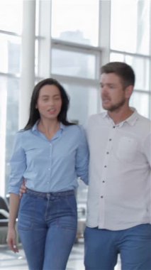 Şık, genç bir çift, neşeli bir şekilde araba galerisinde geziniyor, sakallı adam, sevgilinin kalçasında elini şefkatle dinlendiriyor. Parlak gülümsemeleri ve çeşitli gösterişli araçlar hakkındaki canlı tartışmaları bir atmosfer yaratıyor.