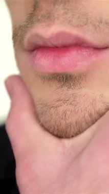 Cesur genç bir adam aynanın karşısında duruyor, tek eliyle çenesini nazikçe okşuyor, özgüven ve cazibe saçıyor. Tişörtsüz görünüşü, heykeltraş köpüğü, yeni ve şık bir tımar rutininin vücut bulmuş hali.