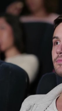 Odaklanmış genç bir adam pofuduk bir sinema koltuğunda oturur, büyük ekrandaki sürükleyici hikayeye kendini kaptırırken gözleri heyecandan genişler. Yakınlardaki arkadaşlar patlamış mısır ve gazozu paylaşıyor, kahkahaları samimi tiyatroda yankılanıyor, canlı bir hava yaratıyor.