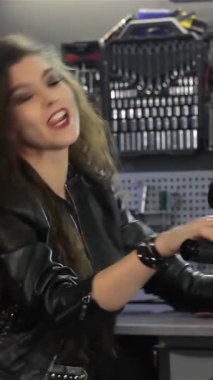 Canlı, genç, beyaz bir kadın canlı bir motosiklet atölyesinde neşeli bir şekilde dans ediyor. Kendine güven ve heyecan saçıyor. Kıvırcık saçlarıyla ve kollarını havaya kaldırarak motosikletçi yaşam tarzının özünü yakalıyor.