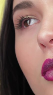 Yetenekli bir vizojist, doğal çekiciliğini vurgulamak için çekici esmer bir kızın dudaklarına zengin erik ruj sürer. Parlak sarı arka plan sıcaklığı yansıtıyor, muhteşem Asyalı kadınların etkileyici gözlerine dikkat çekiyor ve