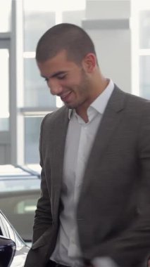 Parlak, modern bir araba galerisinde tutkulu bir araba satıcısı şık giyimli genç bir adama yepyeni bir araba gösteriyor. Satıcı hareketlerle arabaların çarpıcı özelliklerini vurgularken, hava beklentiyle elektriklidir.