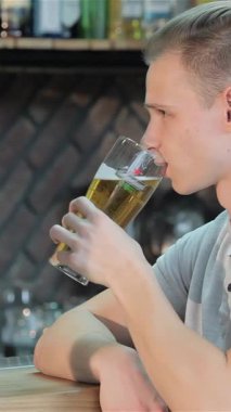 Süslü, sarı saçlı beyaz bir adam soğuk bir bira bardağını kaldırırken, parlak bir ahşap bara yaslanarak neşe saçıyor. Bulaşıcı gülüşü ve gevşek tavırları sıcaklığı yayarak, arkadaşlarını bu coşkulu olaya katılmaya davet ediyor.