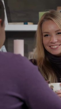 Parlak sarı saçlı genç bir kadın büyüleyici bir kafede erkek arkadaşıyla çay içerken kahkahalarla gülüyor. Çiçek aksanları ve sıcak ışıklandırmayla zenginleşen rahat ortam, hoş bağlantıları için samimi bir zemin oluşturur.