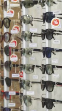 Dalgalı saçlı, şık bir genç kadın moda bir optometriste sergilenen bir dizi şık güneş gözlüğünü tutkuyla fotoğraflıyor. Kırsal tuğla duvarın sıcak renkleri canlı gözlüklerle çok güzel tezat oluşturuyor.