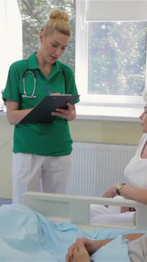 Parlak bir hastane koğuşunda, canlı yeşil önlüklü şefkatli genç bir hemşire erkek bir hasta ve yaşlı karısıyla samimi bir konuşma yapar. Sarışın saçı zarif bir şekilde geriye bağlanmış. Sıcak bir gülümseme ile dolu bir atmosfer yaratıyor.