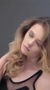 Göz kamaştırıcı beyaz bir kadın, uzun, dalgalı kahverengi saçlarını parlak, gri bir arka plana atıyor, kendine güven ve cazibe saçıyor. Narin elleri her hareketinde büyüleyici güzelliğini gösteren büyüleyici bir zarafet dansı yaratıyor.