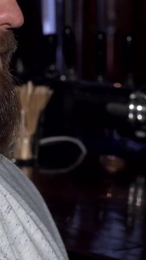 Sakallı bir adam keyifle köpüklü bir biranın tadını çıkarır, mutlu gülüşü rahat bar atmosferini aydınlatır. Sıcak, davetkar renkler ve kırsal dekor bu saf rahatlama ve kutlama anını güçlendirir.