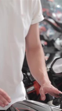 Büyüleyici bir gülümsemesi olan genç beyaz bir adam, parlak benzin deposunu hayranlıkla okşayan, parlak siyah bir motosiklete doğru eğiliyor. Bu dinamik sahne motosikletçiliğin heyecanını yayıyor, hız ve macera tutkusunu yakalıyor.