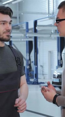 Gösterişli, modern bir atölyede, odaklanmış esmer bir tamirci, gözlük takan genç bir erkek müşteriyle temel araba tamiri hakkında ayrıntılı bir tartışmaya giriyor. El sıkışmaları güven ve profesyonelliği sembolize ediyor, güçlüleri vurguluyorlar.