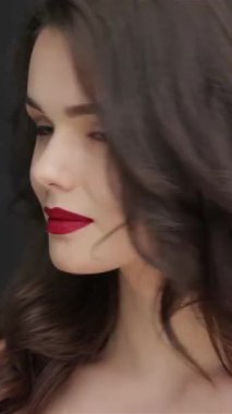 Dalgalı siyah saçları olan büyüleyici genç bir kadın bir öpücük yolluyor büyüleyici gülümsemesi parlak siyah bir arka plana sıcaklık saçıyor. Bu çarpıcı portre onun kusursuz cildini ve koyu kırmızı dudaklarını vurguluyor.