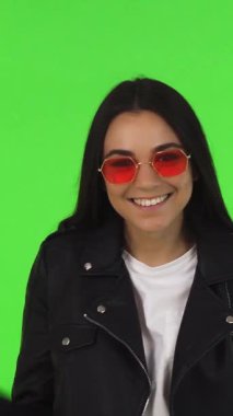 Işıl ışıl, uzun siyah saçlı ve modaya uygun kırmızı güneş gözlüklü bir genç kadın, canlı yeşil bir krom arka planda şık alışveriş torbaları tutuyor. Hevesli onayı güven ve mutluluk yayıyor, mükemmel bir şekilde özetliyor.