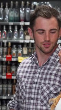 A charming couple engages in a lively discussion while selecting wine in a bustling supermarket aisle, surrounded by colorful bottles and vibrant displays. The handsome young man and his beautiful girlfriend share smiles and thoughtful glances