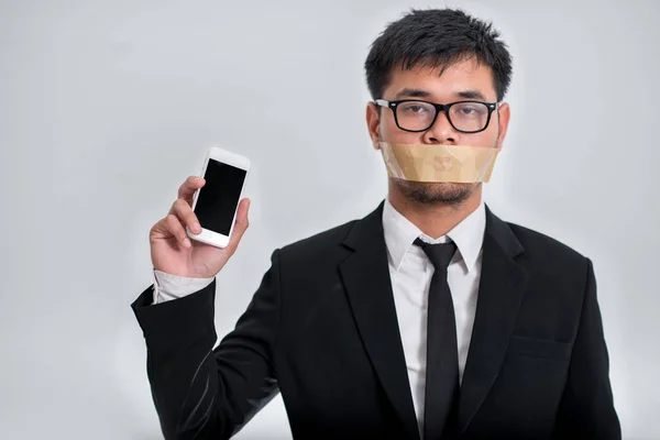 İşadamı ile O'nun silah katlanmış ve O'nun bantlanmış çeneni telefon, koli bandı ağzına gri arka plan üzerinde kapalı alarak işadamı tutan el ile