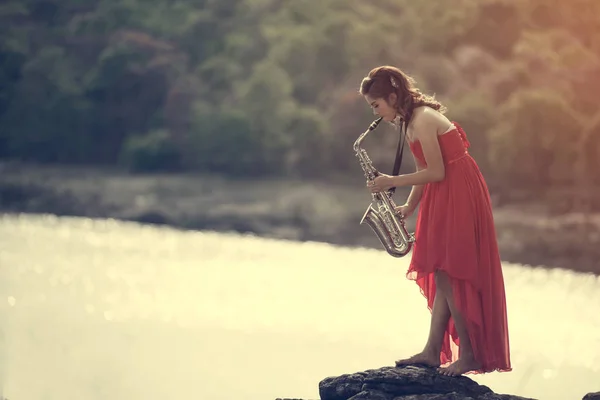 Woman playing saxophone sax at sunset,Saxophonist woman in red dress