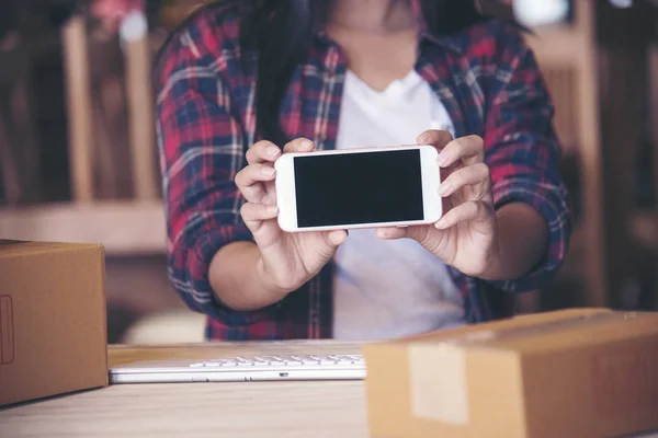 Beautiful woman holding phone,Young entrepreneur, teenager business owner work at home, box for delivery