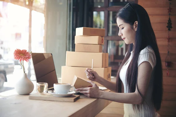 Kahve dükkanı ambalaj arka plan üzerinde çalışan güzel bir kadın. online alışveriş KOBİ girişimci genç kadınlar mutlu çalıştıktan sonra müşteriden yeni sipariş. e-ticaret online kavramı.