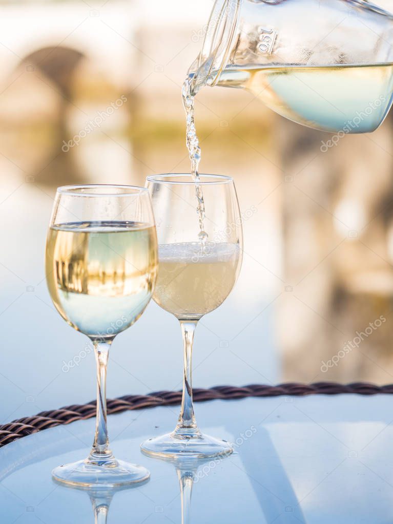 White Portuguese wine pouring from jar to glass on outdoor table by river in Old Town of Tavira, Algarve, Portugal.