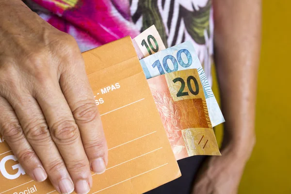 Idosa segurando dinheiro brasileiro para önce sosyal para aposentadoria