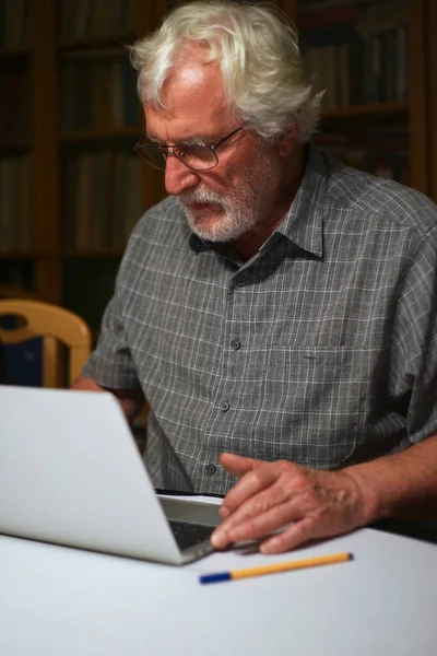 Portrait of a white bearded senior man with grey shirt looking at a laptop, notebook screen.