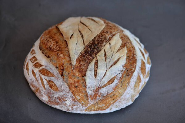 Home baking: crusty sourdough bread on black stone; tree leaves bread scoring 