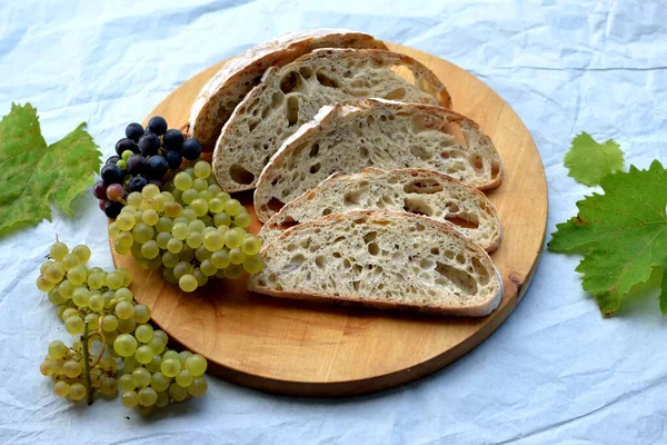 Bread texture of home baked wheat bread with seeds cut in half with bread slices  on wooden board; grapes in background