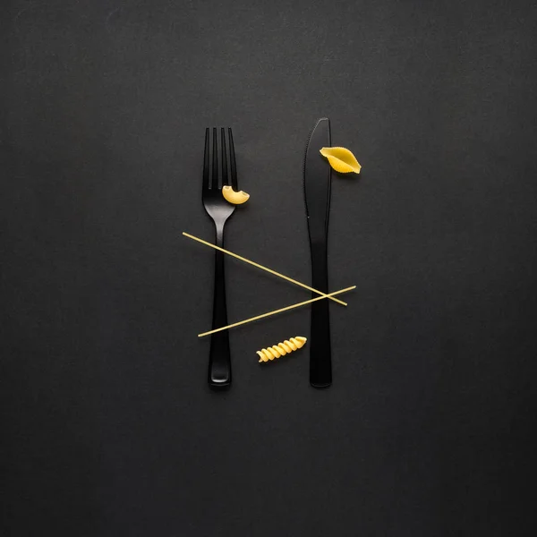 黒い背景に生パスタのスプーンとフォークの創造的な静物写真 — ストック写真
