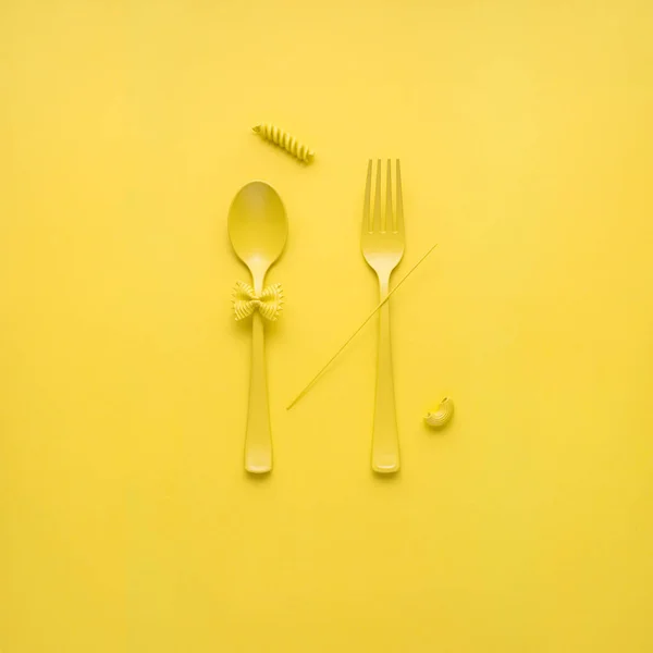 黄色の背景に生パスタをスプーンとフォークの創造的な静物写真 — ストック写真