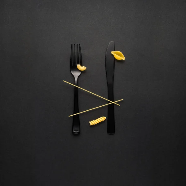 Creative still life photo of fork and spoon with raw pasta on black background. — Stock Image Creative Still Life Photo Fork Spoon Raw Pasta Black Background Stock Image