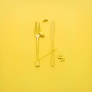 Çatal ve kaşık sarı zemin üzerine pişmemiş makarna ile yaratıcı natürmort fotoğrafı.