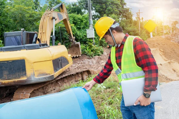 エンジニアは安全制服を着用し 建設現場で大規模なパイプパッチと配管水システムを地下で掘削するラップトップを保持します — ストック写真