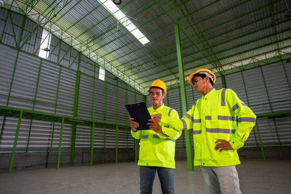 Asian Industrial Engineer in Hard Hat Wearing Safety Jacket plan work with warehouse workers Processes in the factory.