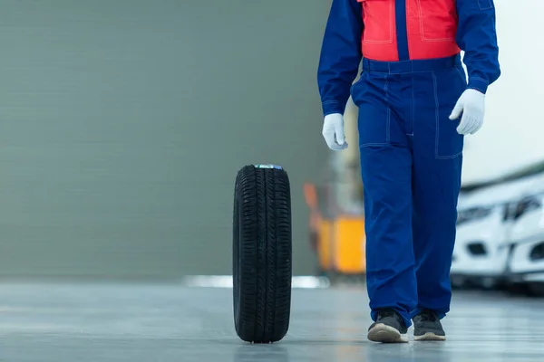 Auto mechanic change tire attractive auto mechanic man in blue uniform with blue gloves rolling wheel going on the autoservice in the auto repair center