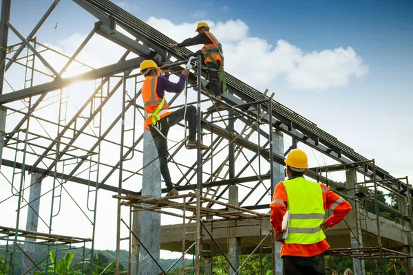 屋根構造物の建設におけるアジアの建設労働者の制御と労働者は屋根をインストールするための安全高さ機器を着用しています 安全ボディハーネスフック付き労働者のための秋の逮捕装置 建設現場の労働者 — ストック写真