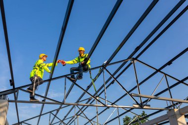 İnşaat alanında güvenlik yüksekliği ekipmanı; Asyalı işçiler çatıyı kurmak için güvenlik yüksekliği ekipmanı takıyorlar. Emniyet kemeri için kancaları olan işçiler için tutuklama aygıtını düşür.